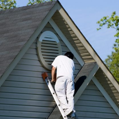 Painter working at the top of an extension ladder on a two story suburban home.